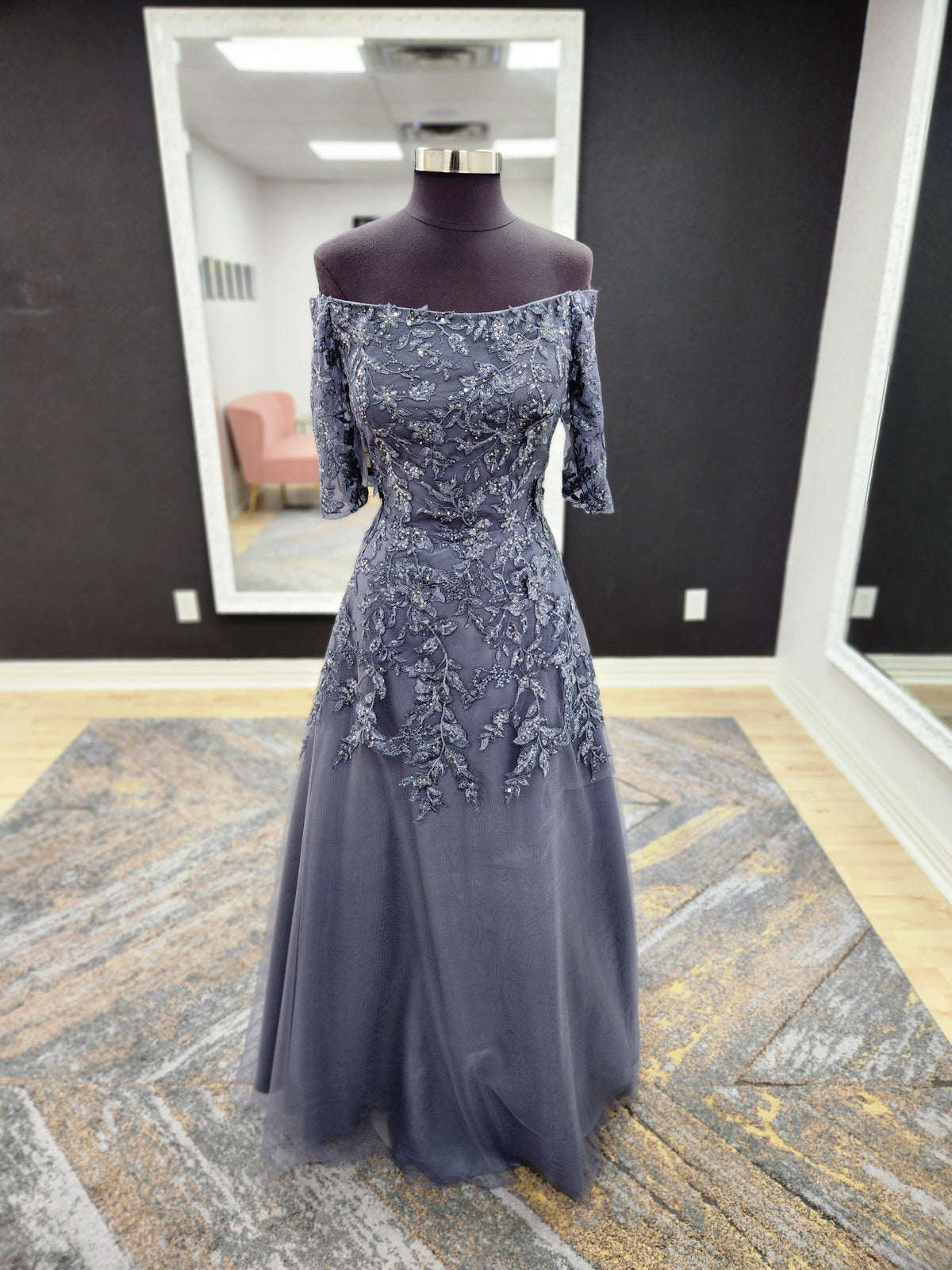 Morilee MGNY 72834 off-the-shoulder mother of the bride gown with embroidered lace bodice, sheer sleeves, and flowing A-line skirt with detachable overskirt.