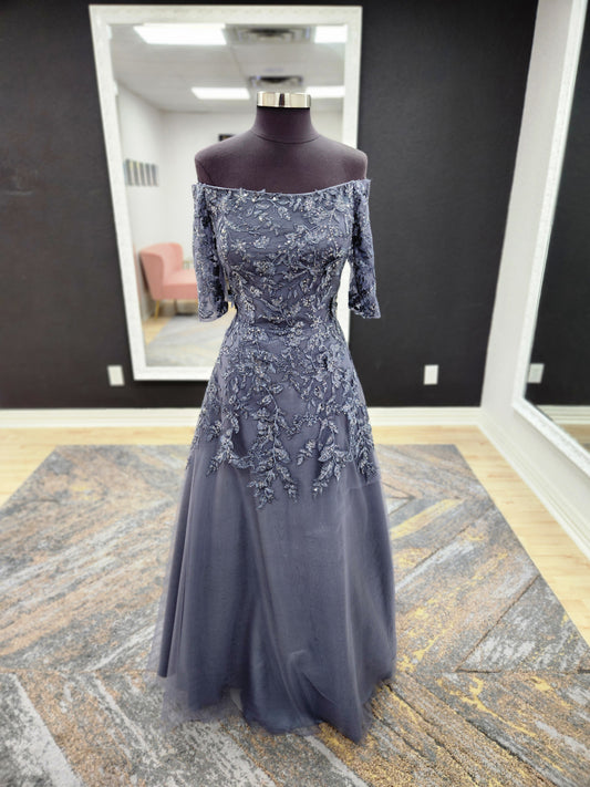 Morilee MGNY 72834 off-the-shoulder mother of the bride gown with embroidered lace bodice, sheer sleeves, and flowing A-line skirt with detachable overskirt.
