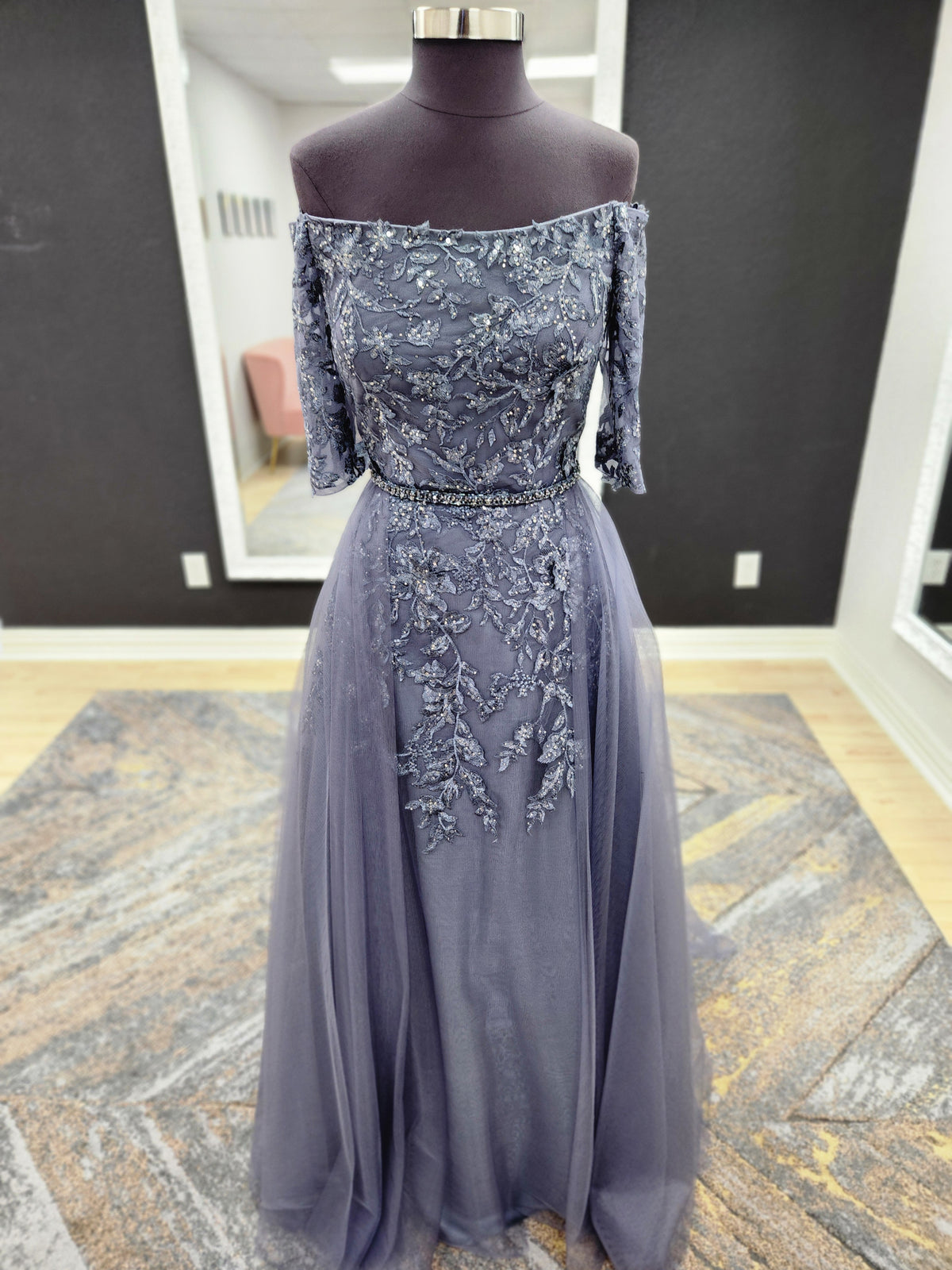 Morilee MGNY 72834 off-the-shoulder mother of the bride gown with embroidered lace bodice, sheer sleeves, and flowing A-line skirt with detachable overskirt.