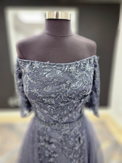 Morilee MGNY 72834 off-the-shoulder mother of the bride gown with embroidered lace bodice, sheer sleeves, and flowing A-line skirt with detachable overskirt.