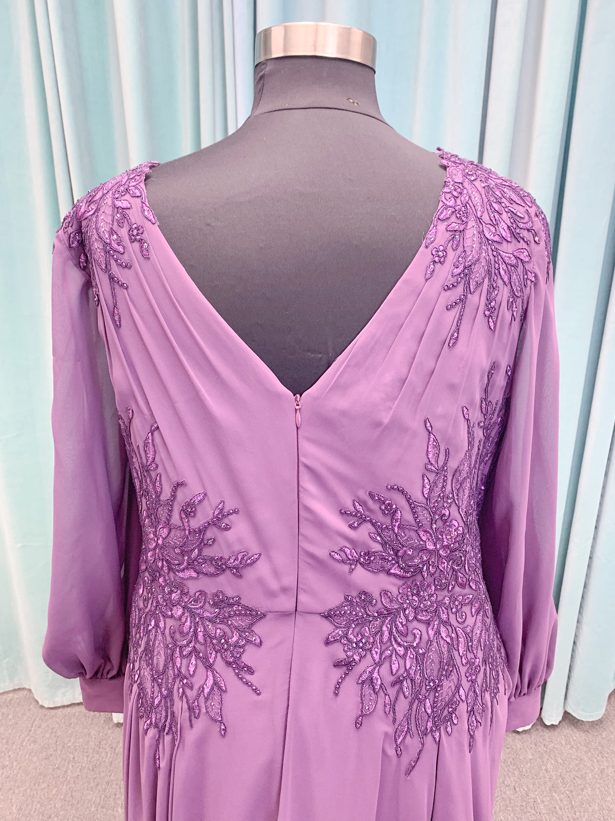 Morilee MLNY 72717 plus size A-line mother of the bride dress on mannequin with draped V-neckline, sheer bishop sleeves, beaded lace appliques at the shoulders and waist, and flowing chiffon skirt with sweep train