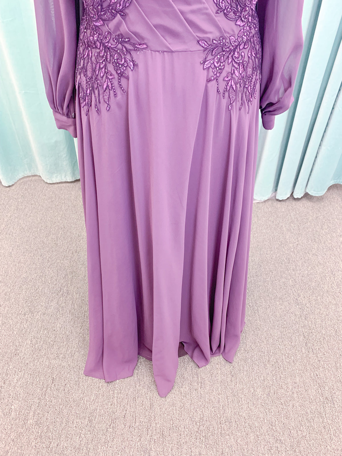 Morilee MLNY 72717 plus size A-line mother of the bride dress on mannequin with draped V-neckline, sheer bishop sleeves, beaded lace appliques at the shoulders and waist, and flowing chiffon skirt with sweep train