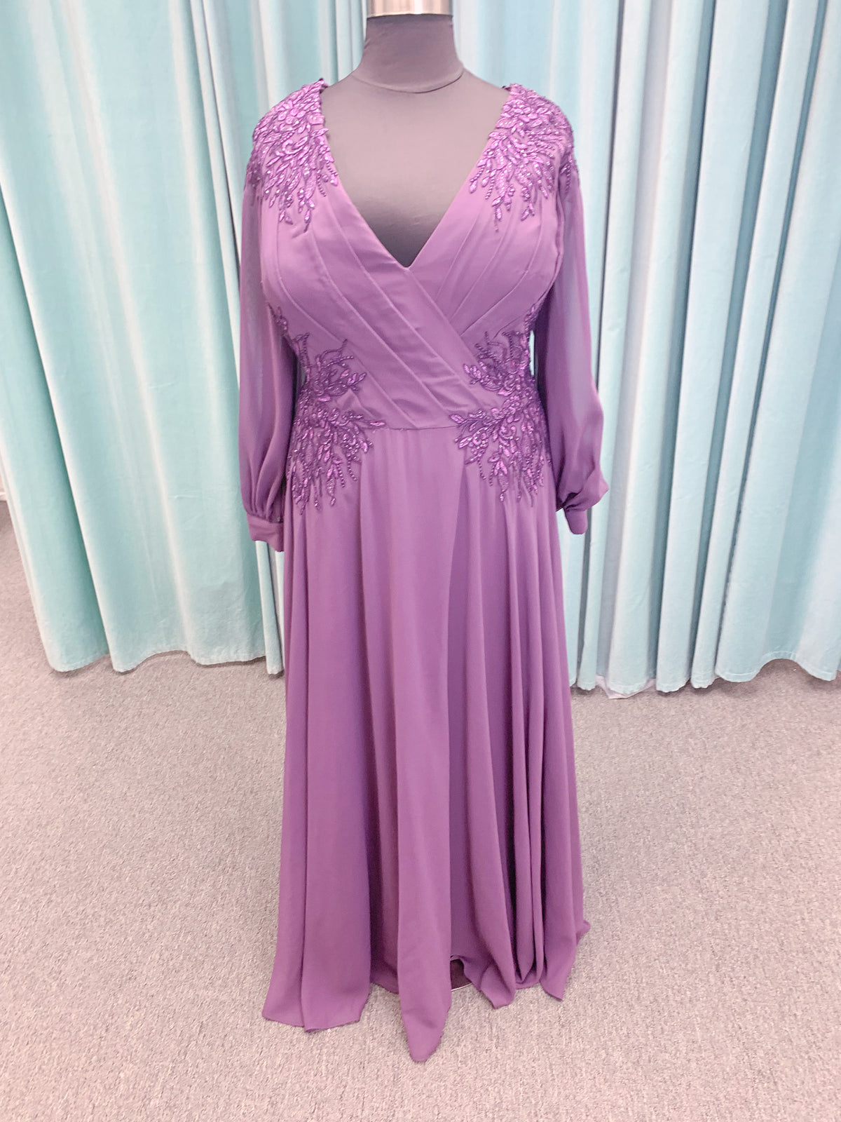 Morilee MLNY 72717 plus size A-line mother of the bride dress on mannequin with draped V-neckline, sheer bishop sleeves, beaded lace appliques at the shoulders and waist, and flowing chiffon skirt with sweep train