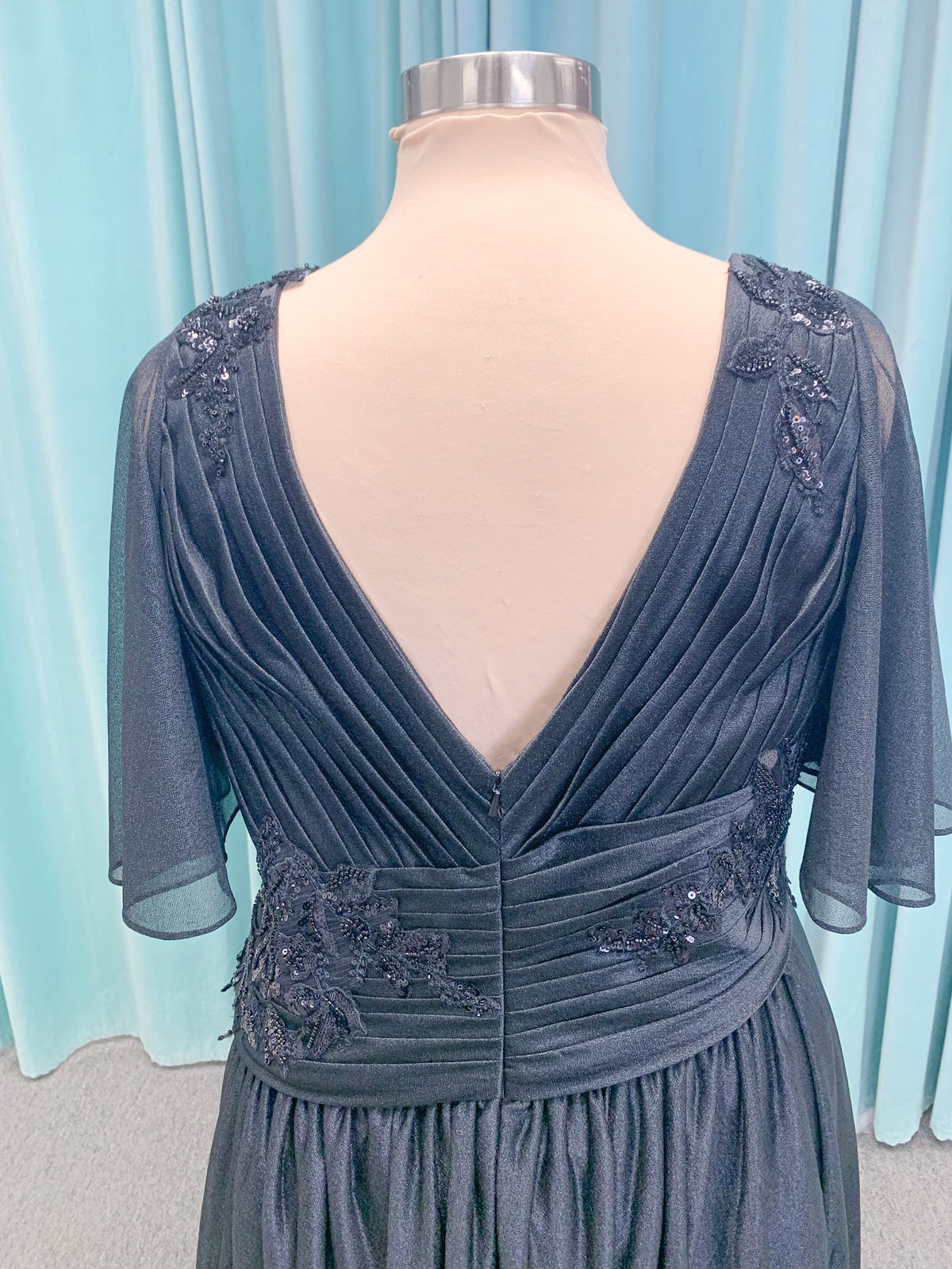 Morilee MLNY 73102 plus size A-line mother of the bride dress on mannequin with asymmetrically draped V-neck bodice, flutter sleeves, embroidered beaded appliques, and shimmer mesh A-line skirt