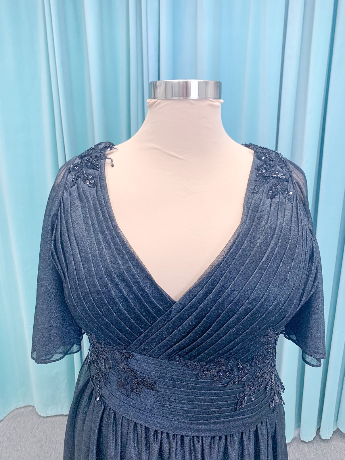 Morilee MLNY 73102 plus size A-line mother of the bride dress on mannequin with asymmetrically draped V-neck bodice, flutter sleeves, embroidered beaded appliques, and shimmer mesh A-line skirt