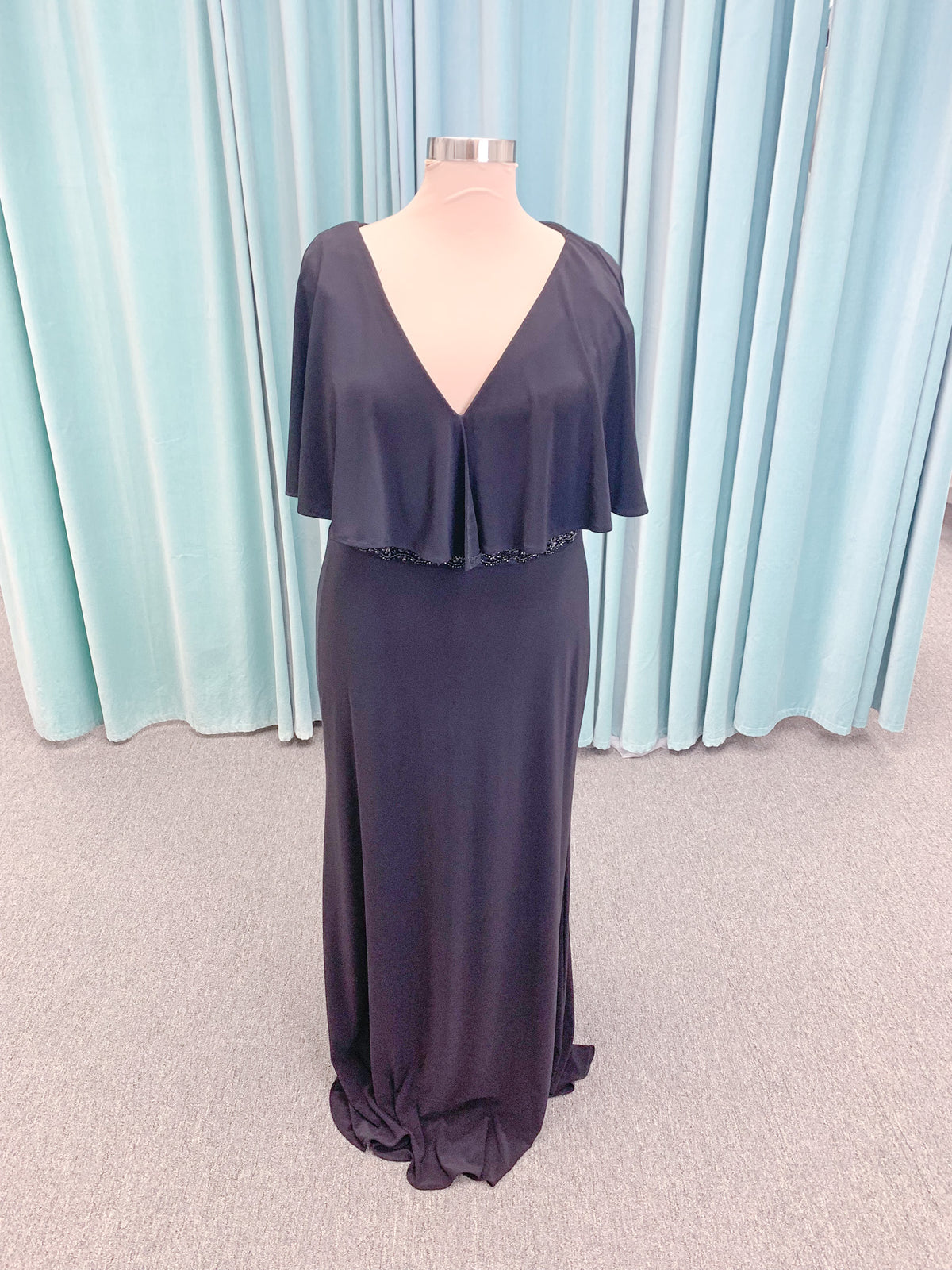 Morilee MLNY 73124 sheath mother of the bride dress on mannequin with V-neckline, flowing capelet overlay, crystal beaded waistband, and slim jersey sheath skirt