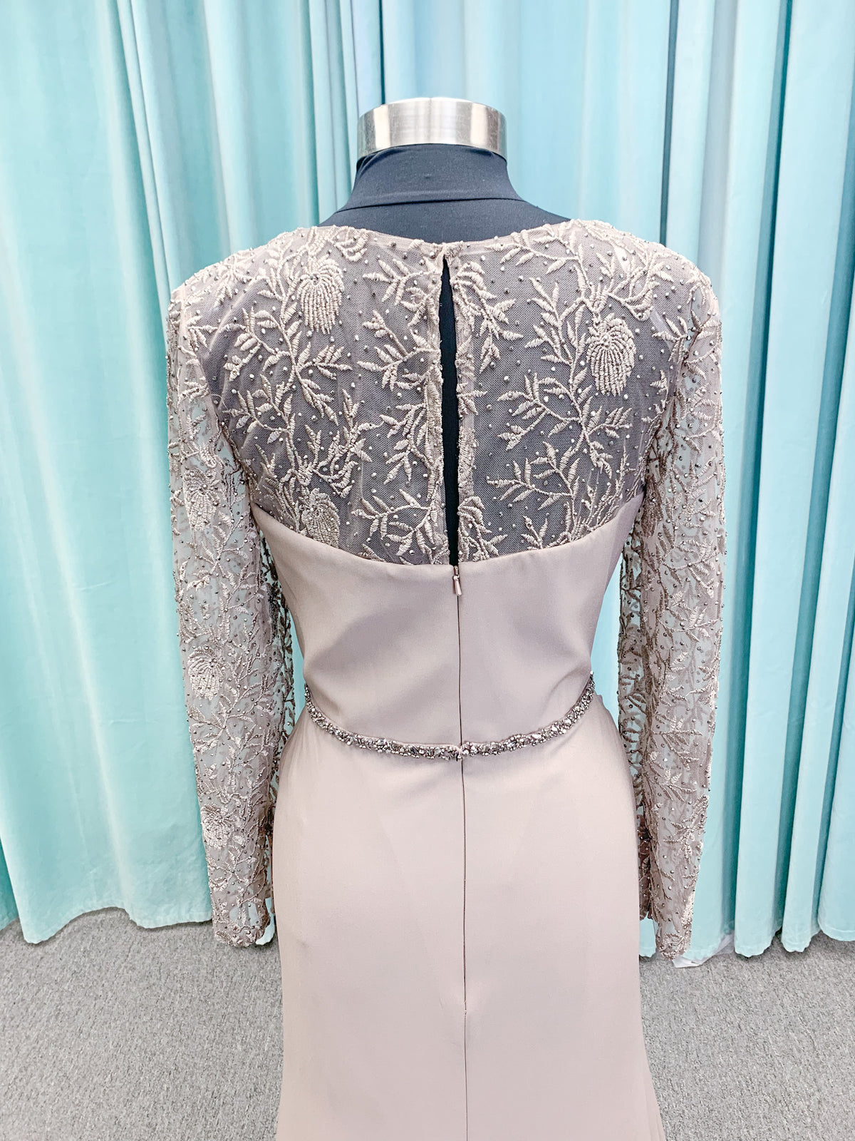 Morilee MLNY 73160 sheath mother of the bride dress on mannequin with modified sweetheart neckline, draped crepe bodice, sheer illusion long sleeves with lace applique, detachable beaded belt, and keyhole back