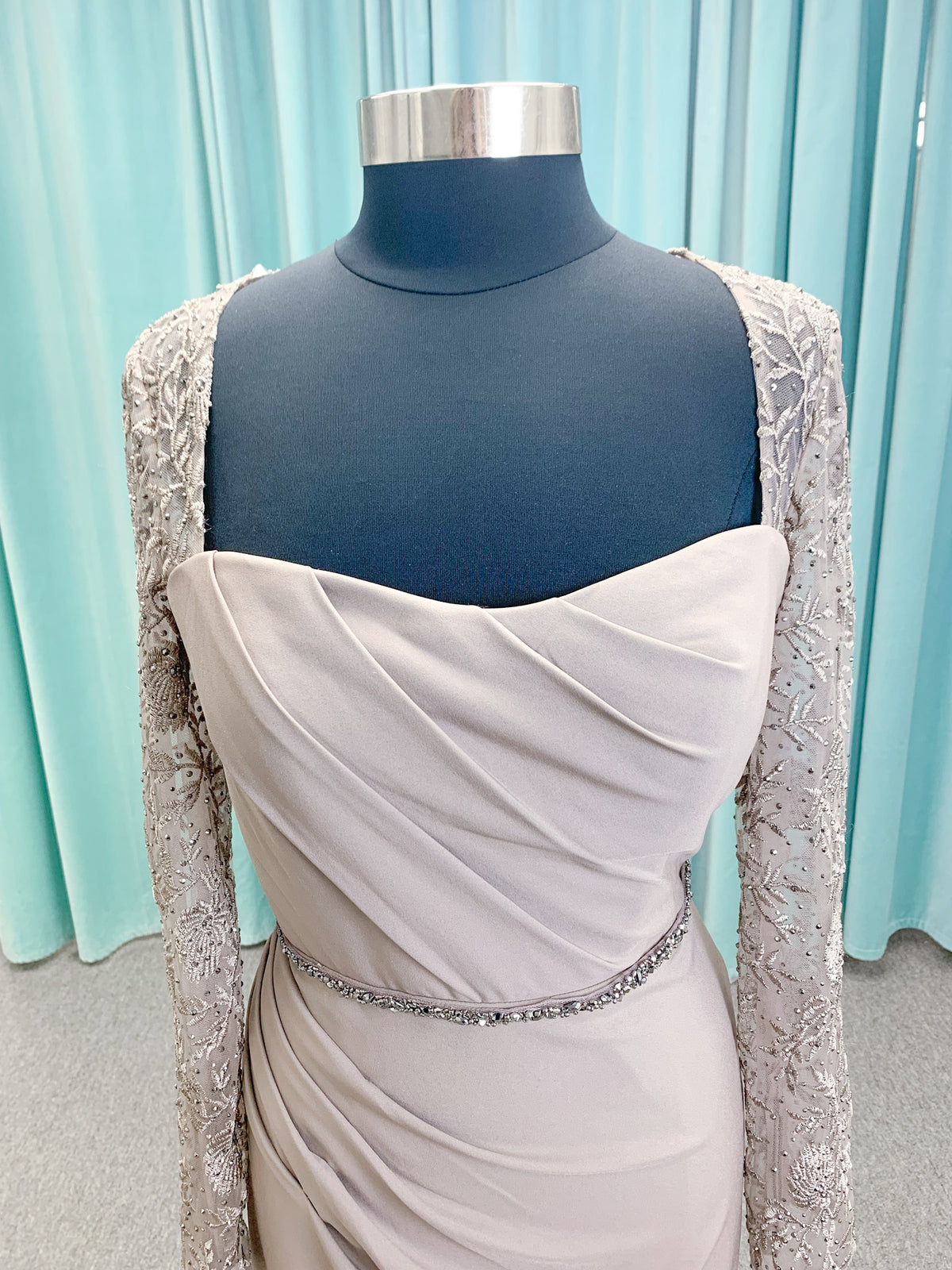 Morilee MLNY 73160 sheath mother of the bride dress on mannequin with modified sweetheart neckline, draped crepe bodice, sheer illusion long sleeves with lace applique, detachable beaded belt, and keyhole back