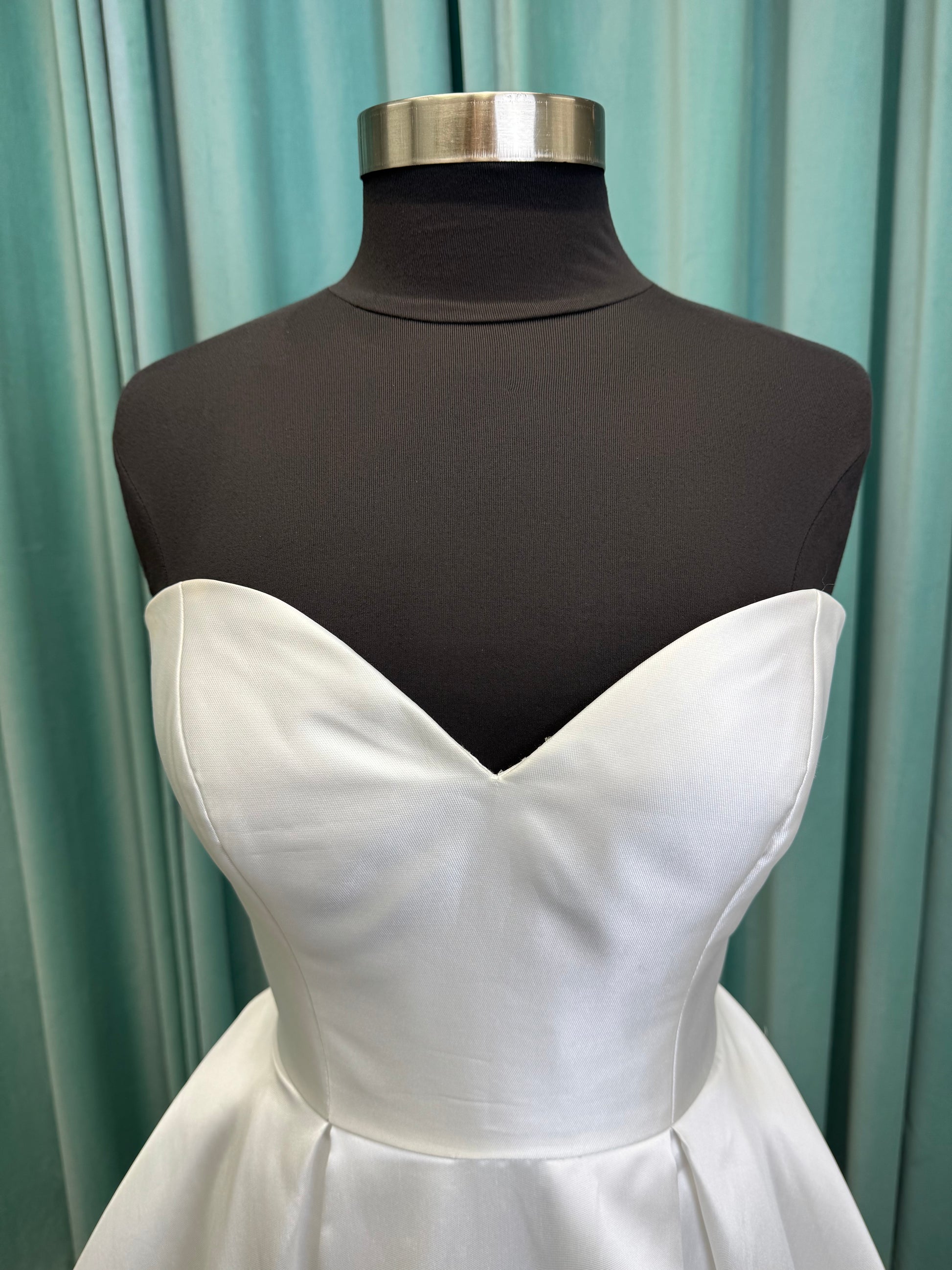 Achelios ivory strapless sweetheart satin ballgown wedding dress on mannequin with full skirt and clean structured bodice.
