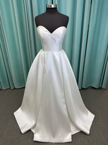 Achelios ivory strapless sweetheart satin ballgown wedding dress on mannequin with full skirt and clean structured bodice.
