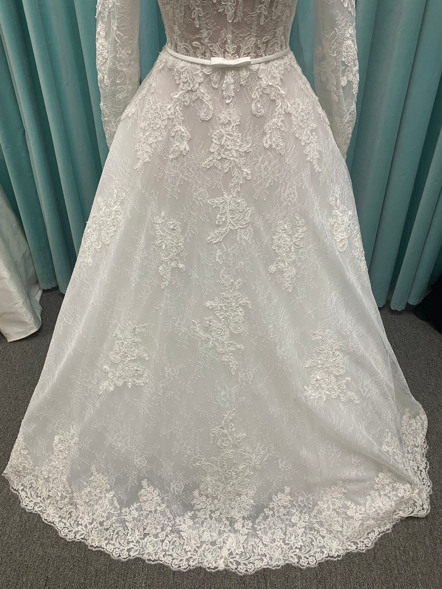 Morilee Sannah 2750 ball gown with strapless sweetheart neckline, lace corset bodice, satin bow waistband, and full tulle skirt with scalloped hem and long sleeves