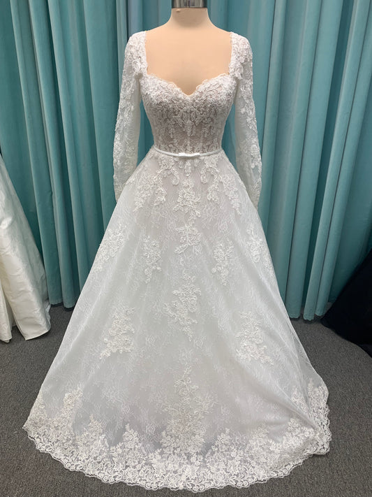 Morilee Sannah 2750 ball gown with strapless sweetheart neckline, lace corset bodice, satin bow waistband, and full tulle skirt with scalloped hem and long sleeves