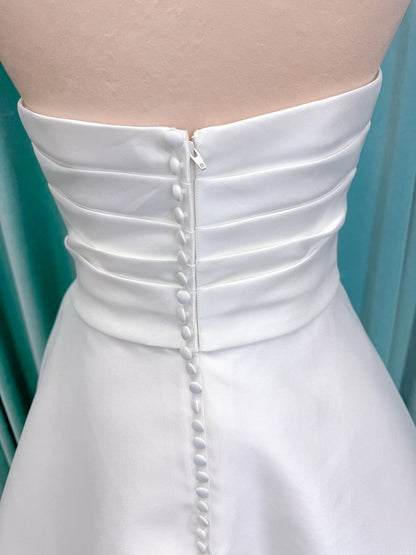 Moonlight Bridal J6852 Artemis A-line wedding dress on mannequin with strapless pointed sweetheart neckline, ruched mikado bodice, natural waist, pleated skirt with front slit, and sweep train