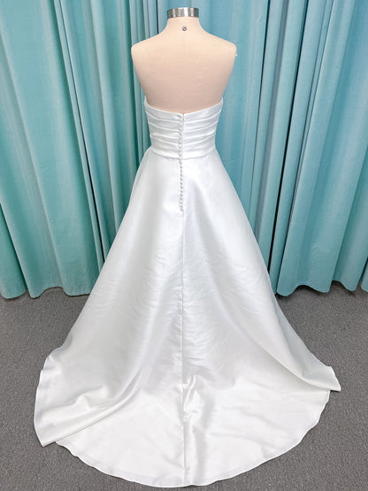 Moonlight Bridal J6852 Artemis A-line wedding dress on mannequin with strapless pointed sweetheart neckline, ruched mikado bodice, natural waist, pleated skirt with front slit, and sweep train
