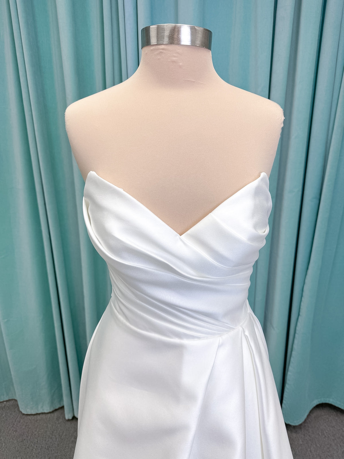 Moonlight Bridal J6852 Artemis A-line wedding dress on mannequin with strapless pointed sweetheart neckline, ruched mikado bodice, natural waist, pleated skirt with front slit, and sweep train
