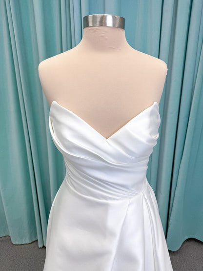 Moonlight Bridal J6852 Artemis A-line wedding dress on mannequin with strapless pointed sweetheart neckline, ruched mikado bodice, natural waist, pleated skirt with front slit, and sweep train
