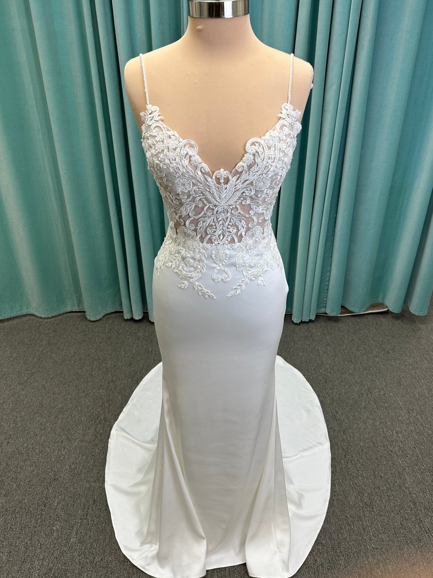 Calliope ivory spaghetti strap V-neck fit-and-flare wedding dress on mannequin with 3D floral lace appliqué bodice and sleek crepe skirt.
