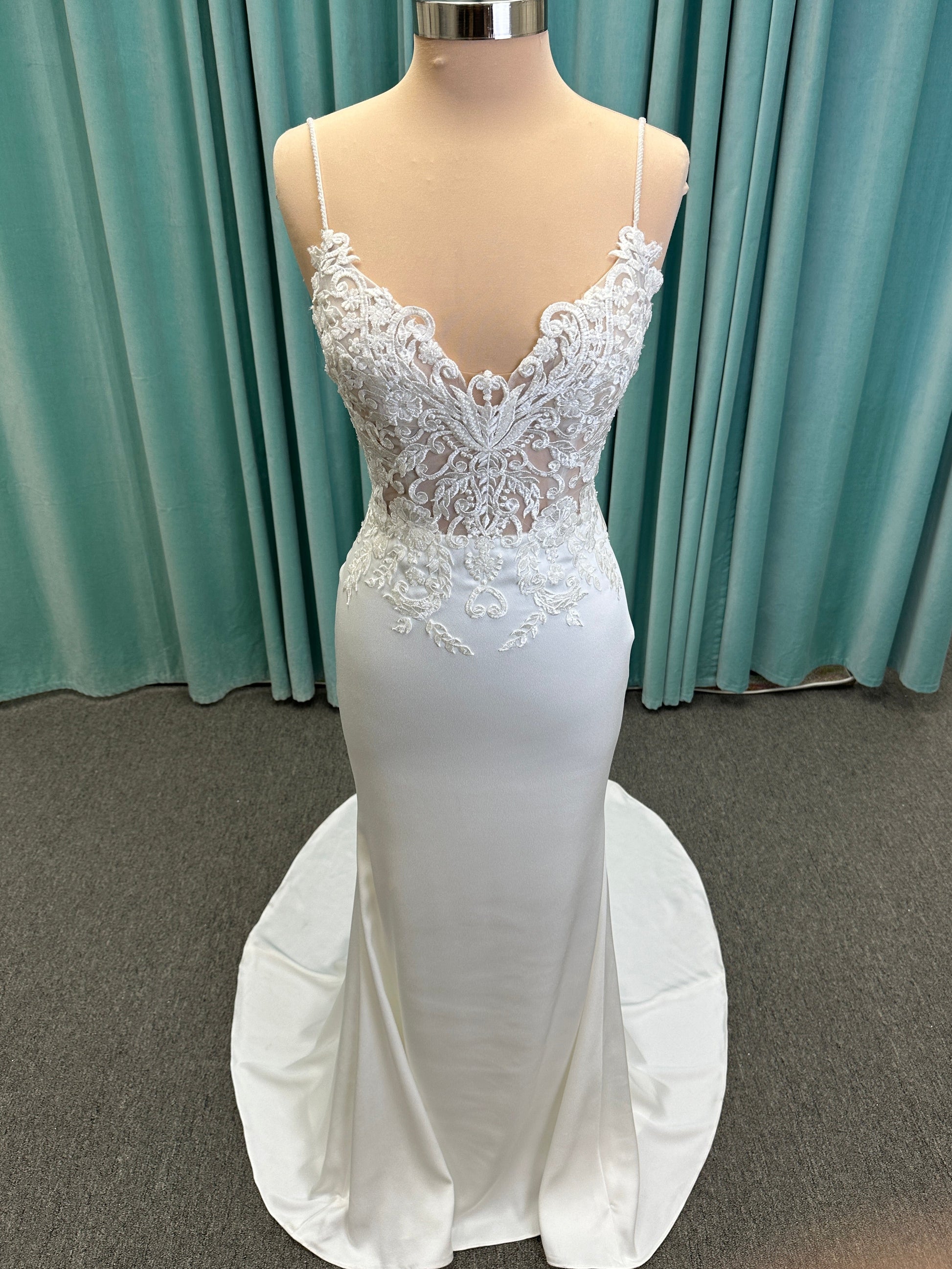 Calliope ivory spaghetti strap V-neck fit-and-flare wedding dress on mannequin with 3D floral lace appliqué bodice and sleek crepe skirt.
