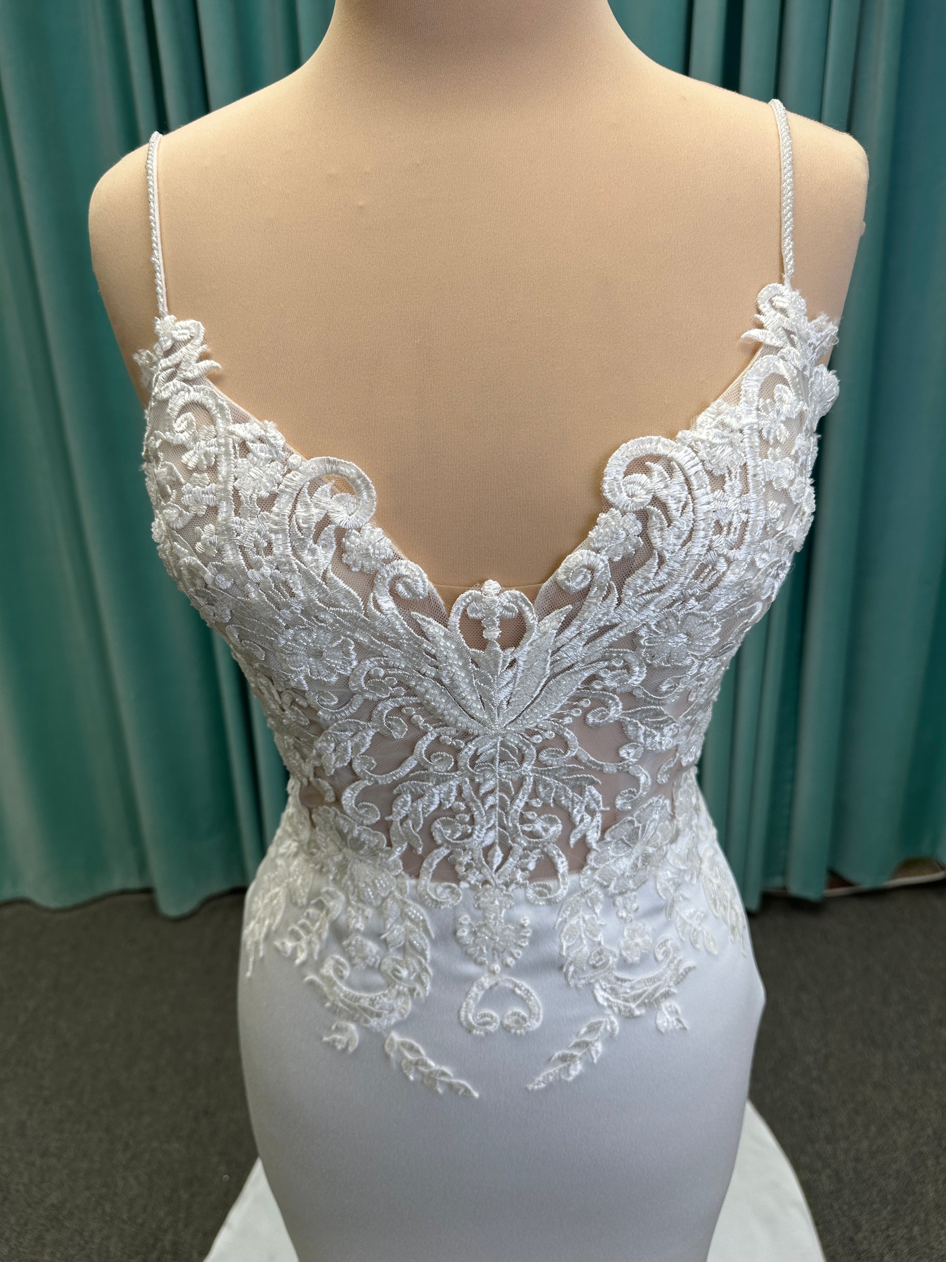 Calliope ivory spaghetti strap V-neck fit-and-flare wedding dress on mannequin with 3D floral lace appliqué bodice and sleek crepe skirt.
