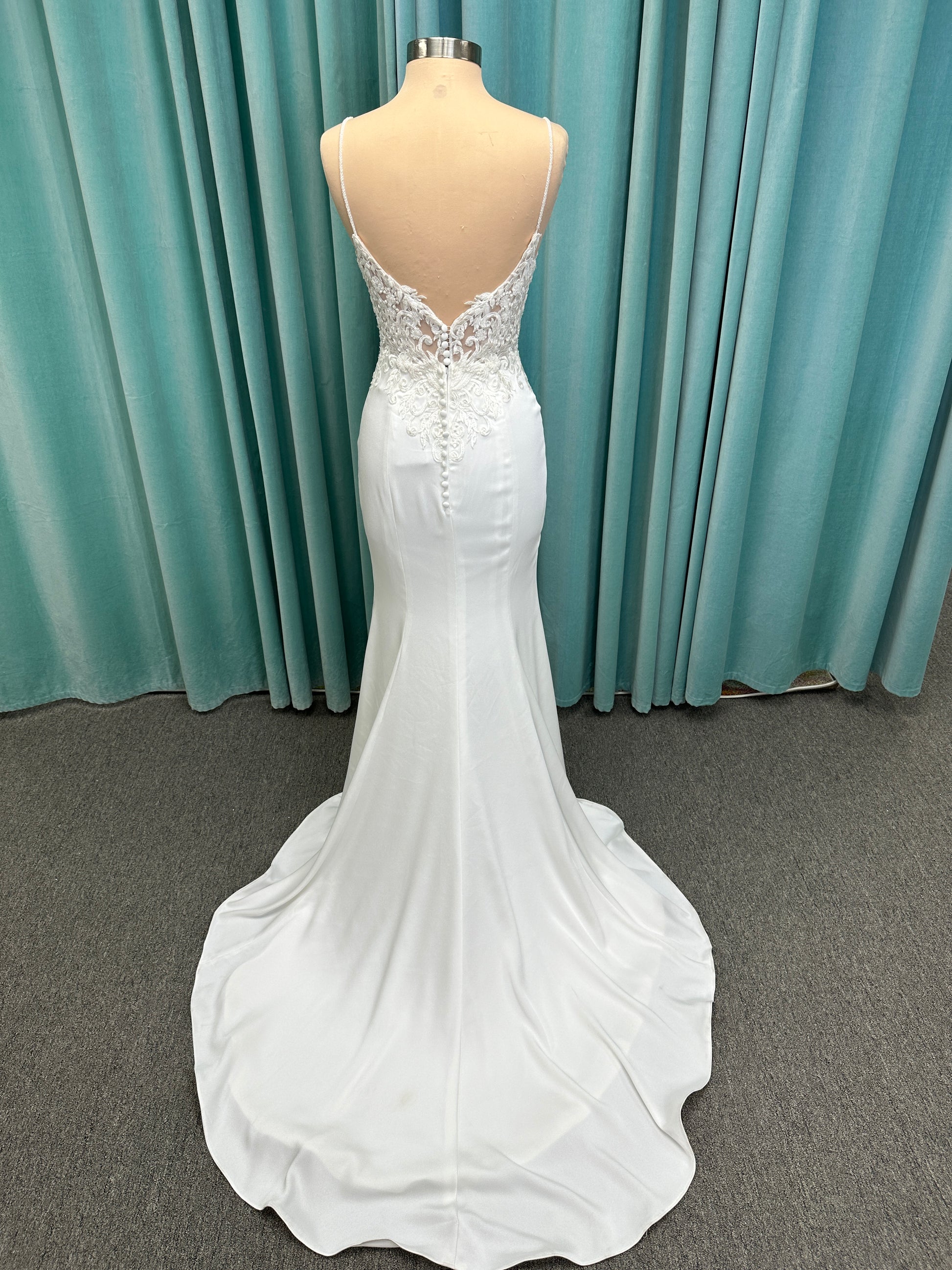 Calliope ivory spaghetti strap V-neck fit-and-flare wedding dress on mannequin with 3D floral lace appliqué bodice and sleek crepe skirt.
