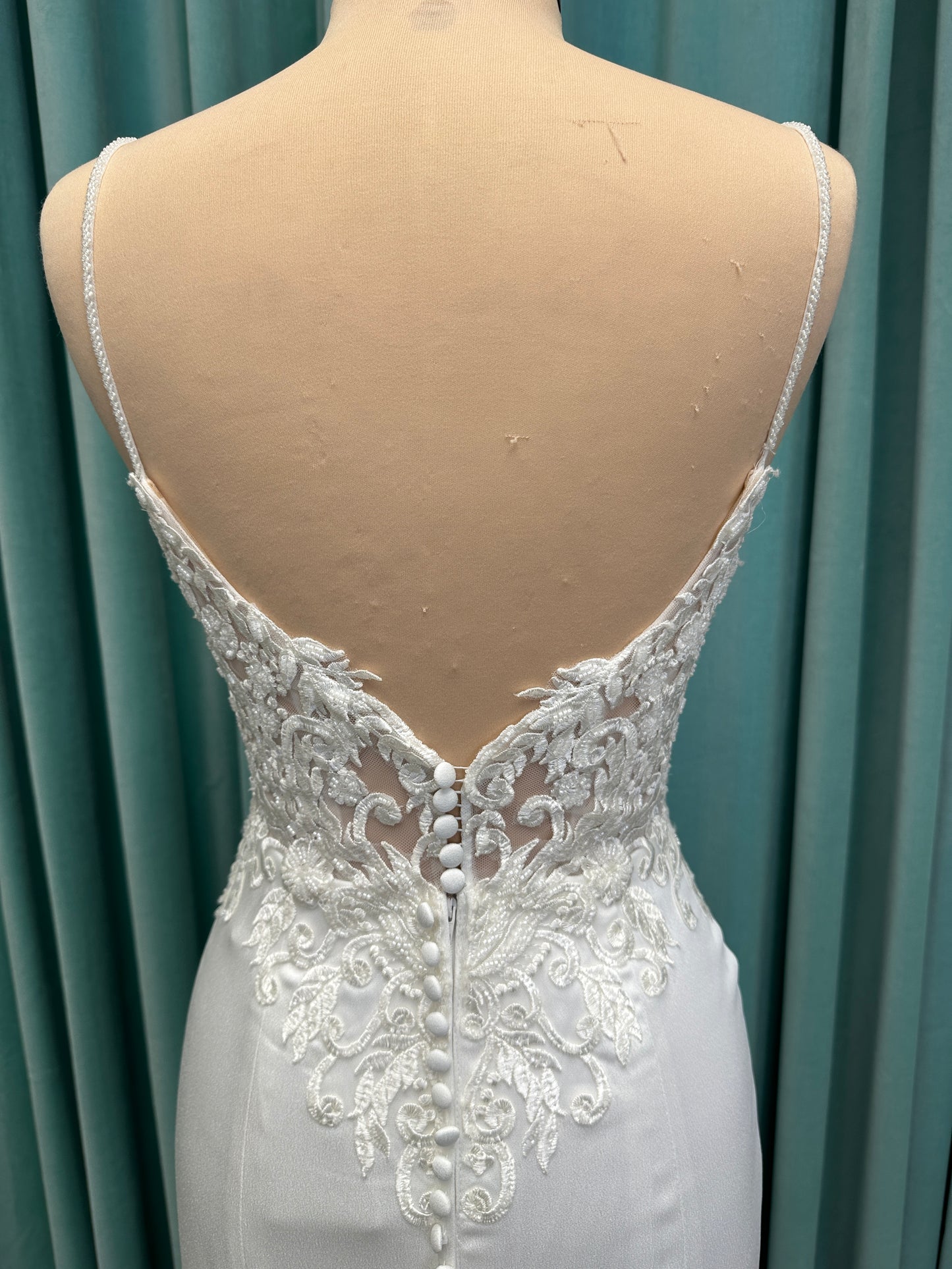 Calliope ivory spaghetti strap V-neck fit-and-flare wedding dress on mannequin with 3D floral lace appliqué bodice and sleek crepe skirt.
