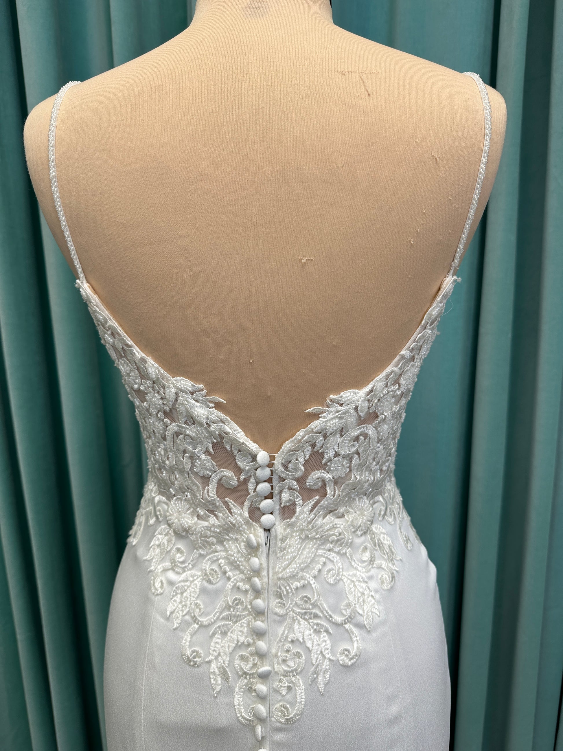 Calliope ivory spaghetti strap V-neck fit-and-flare wedding dress on mannequin with 3D floral lace appliqué bodice and sleek crepe skirt.
