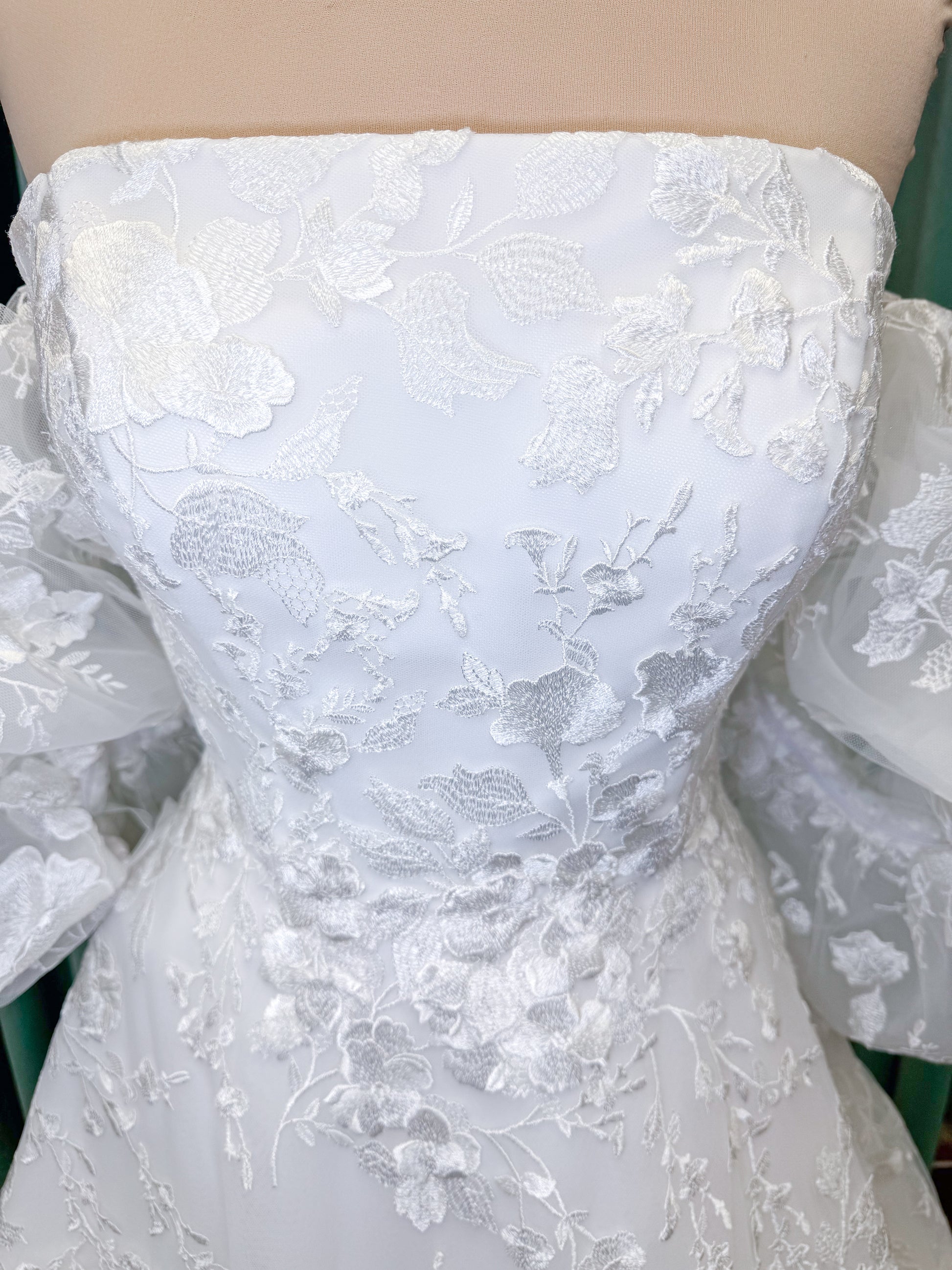 Morilee 2987 Callyso A-line wedding dress on mannequin with strapless tulle, floral threadwork, detachable puff sleeves, and flowing train