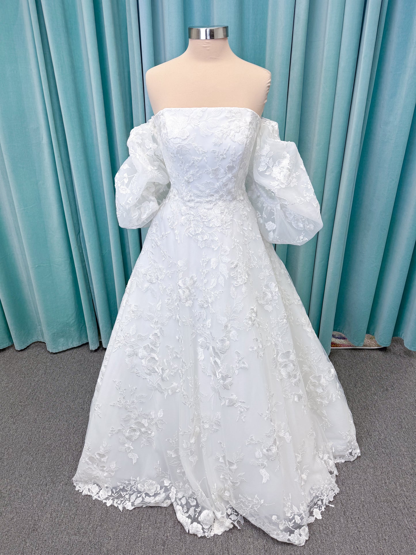 Morilee 2987 Callyso A-line wedding dress on mannequin with strapless tulle, floral threadwork, detachable puff sleeves, and flowing train