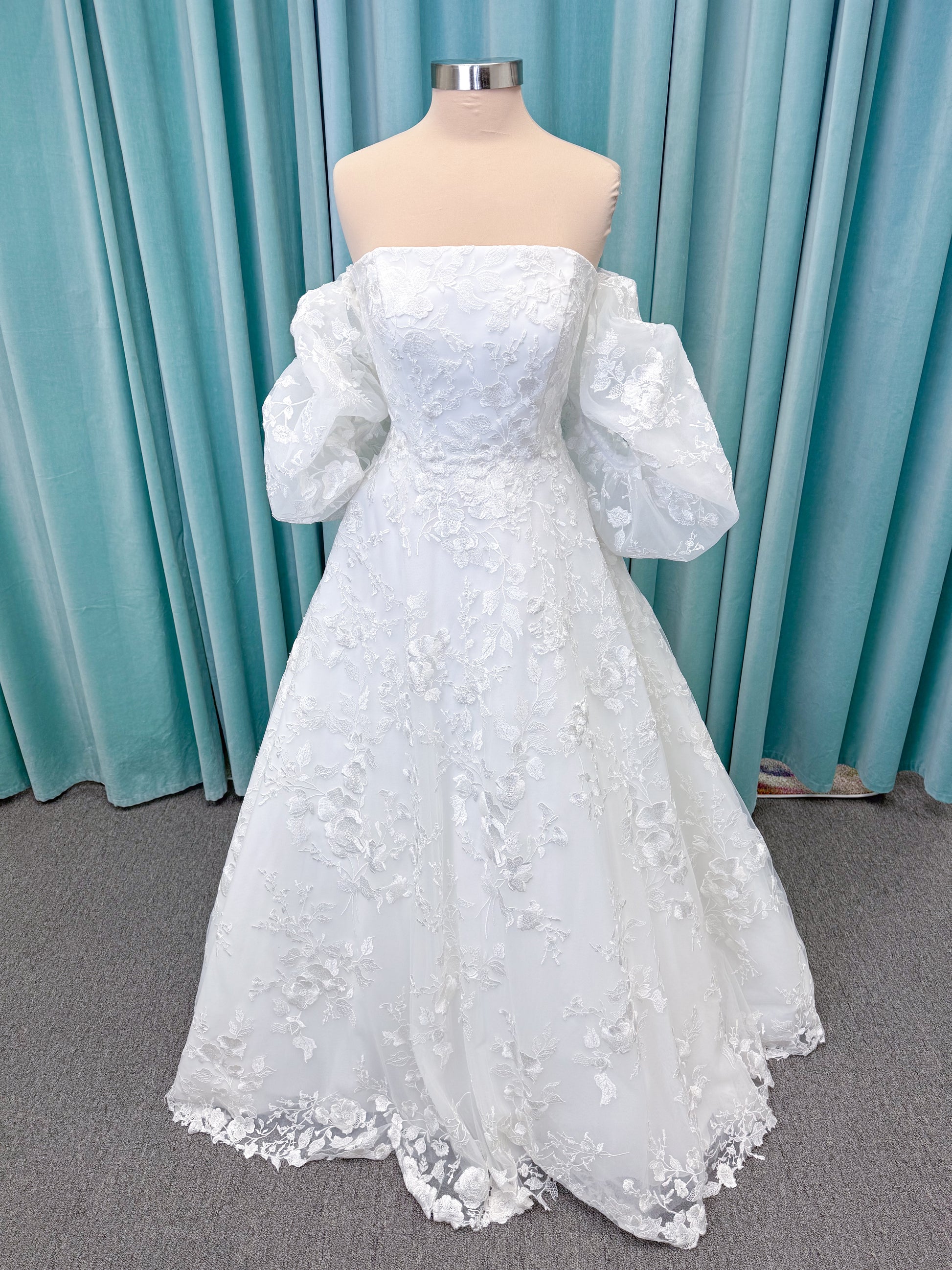 Morilee 2987 Callyso A-line wedding dress on mannequin with strapless tulle, floral threadwork, detachable puff sleeves, and flowing train