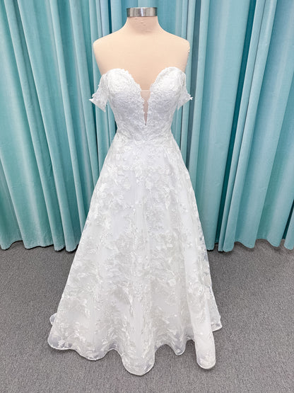 Moonlight Bridal J6818 Channary A-line wedding dress on mannequin with sweetheart illusion neckline, large floral embroidered lace with sequins, off-the-shoulder lace swag sleeves, full net skirt, and chapel train