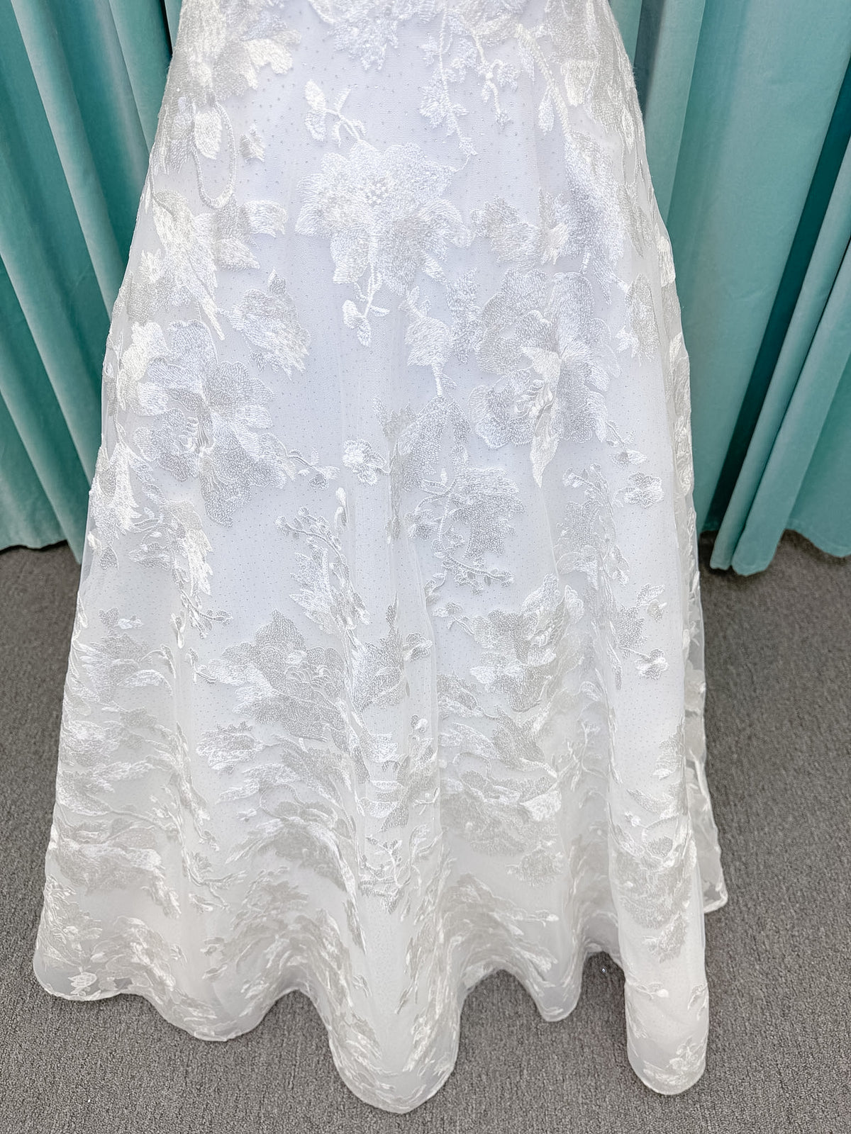 Moonlight Bridal J6818 Channary A-line wedding dress on mannequin with sweetheart illusion neckline, large floral embroidered lace with sequins, off-the-shoulder lace swag sleeves, full net skirt, and chapel train
