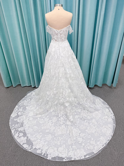 Moonlight Bridal J6818 Channary A-line wedding dress on mannequin with sweetheart illusion neckline, large floral embroidered lace with sequins, off-the-shoulder lace swag sleeves, full net skirt, and chapel train