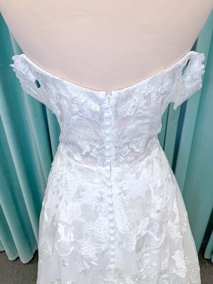 Moonlight Bridal J6818 Channary A-line wedding dress on mannequin with sweetheart illusion neckline, large floral embroidered lace with sequins, off-the-shoulder lace swag sleeves, full net skirt, and chapel train