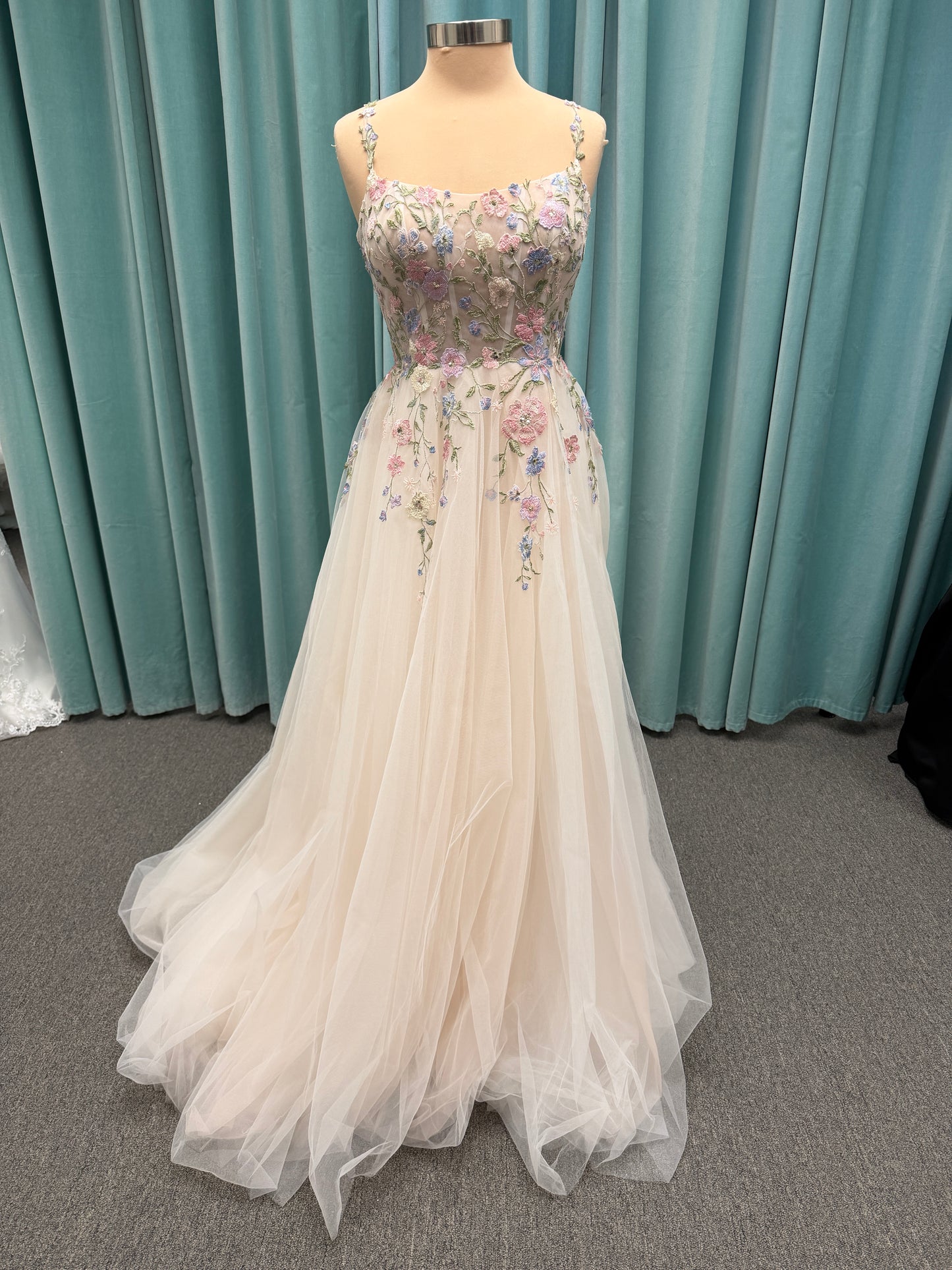Stella York 8063 ivory and pastel colorful embroidered lace A-line wedding dress on mannequin with floral spaghetti straps, scoop neckline, and soft tulle skirt.
