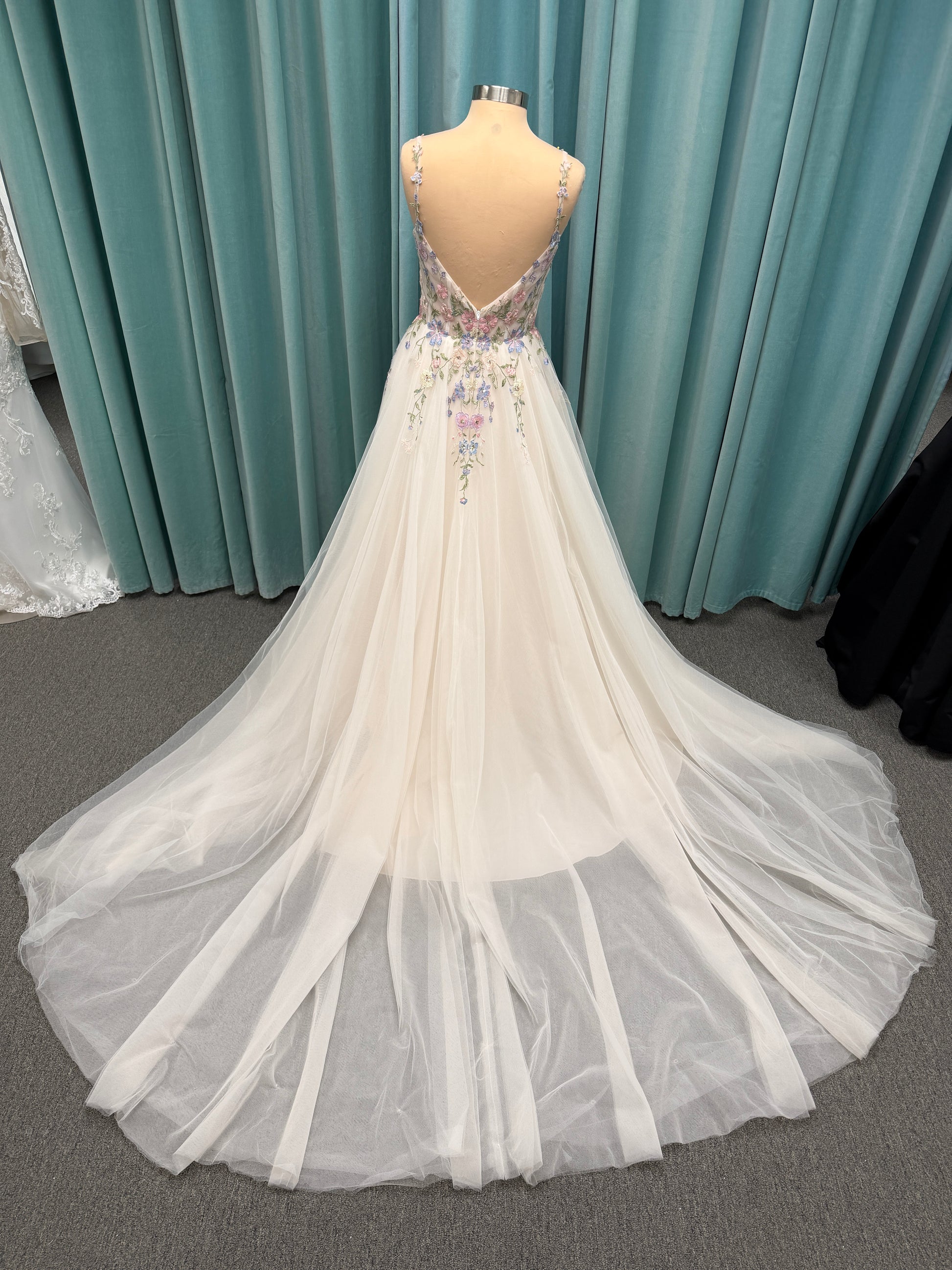 Stella York 8063 ivory and pastel colorful embroidered lace A-line wedding dress on mannequin with floral spaghetti straps, scoop neckline, and soft tulle skirt.
