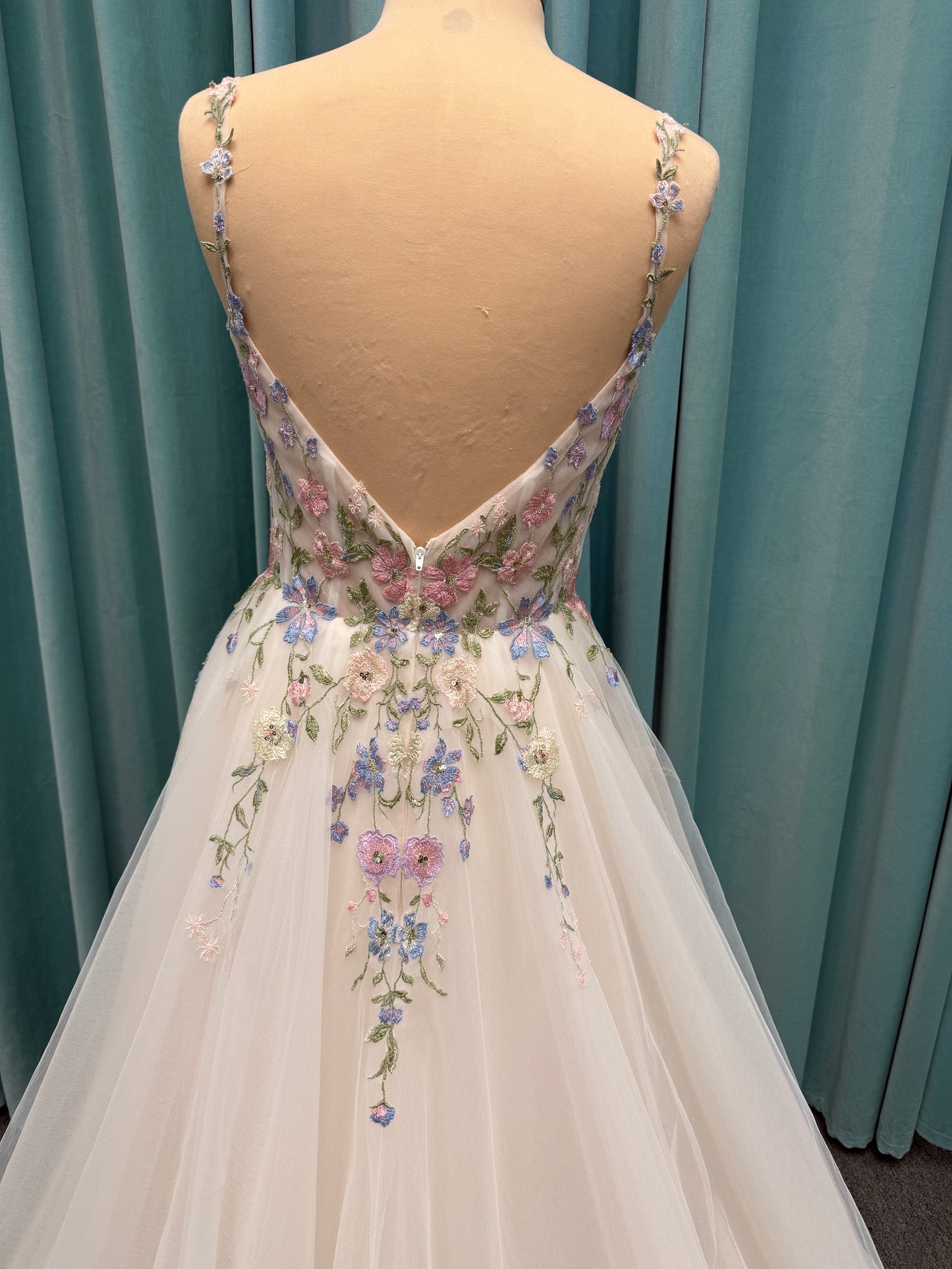 Stella York 8063 ivory and pastel colorful embroidered lace A-line wedding dress on mannequin with floral spaghetti straps, scoop neckline, and soft tulle skirt.
