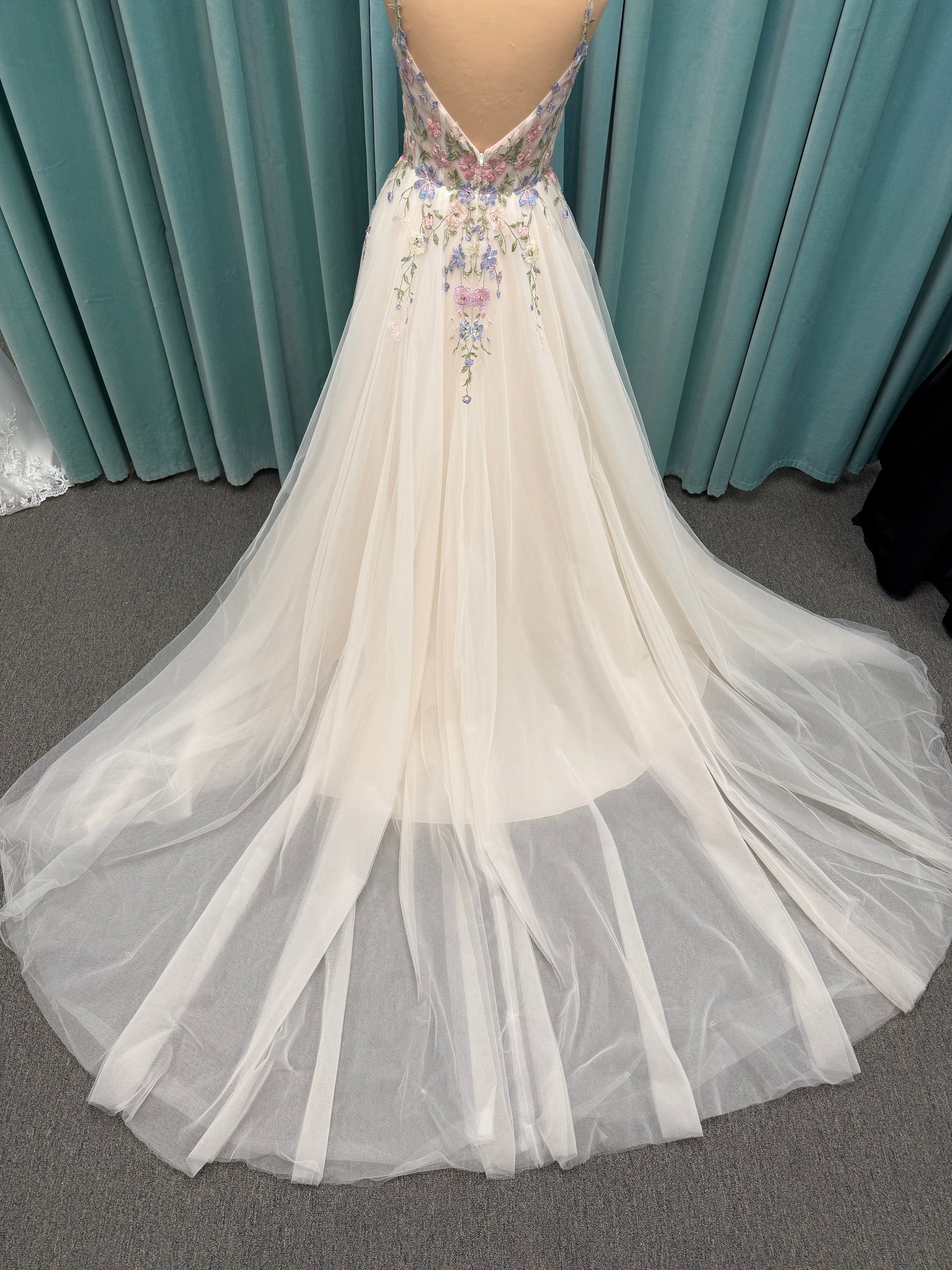 Stella York 8063 ivory and pastel colorful embroidered lace A-line wedding dress on mannequin with floral spaghetti straps, scoop neckline, and soft tulle skirt.
