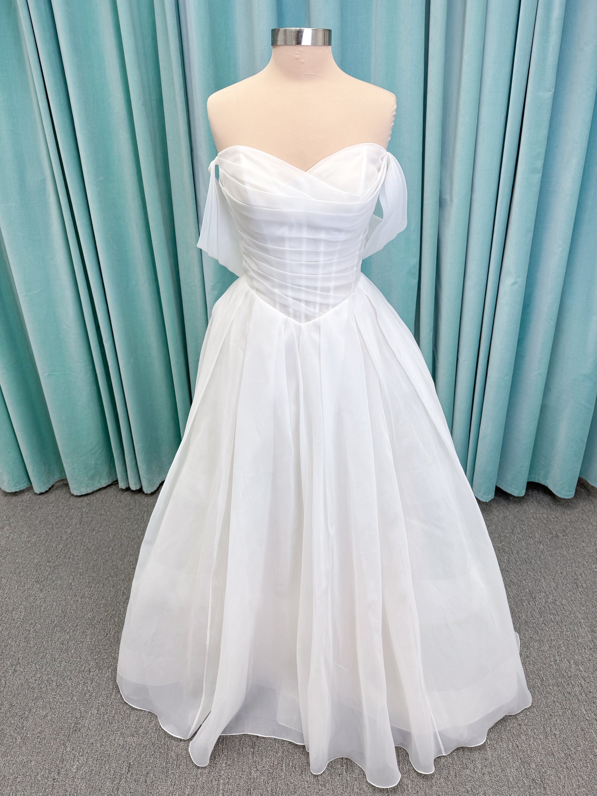 Morilee 2947L Damara A-line wedding dress on mannequin with modified sweetheart neckline, off-the-shoulder detailing, organza box pleats, and corset back