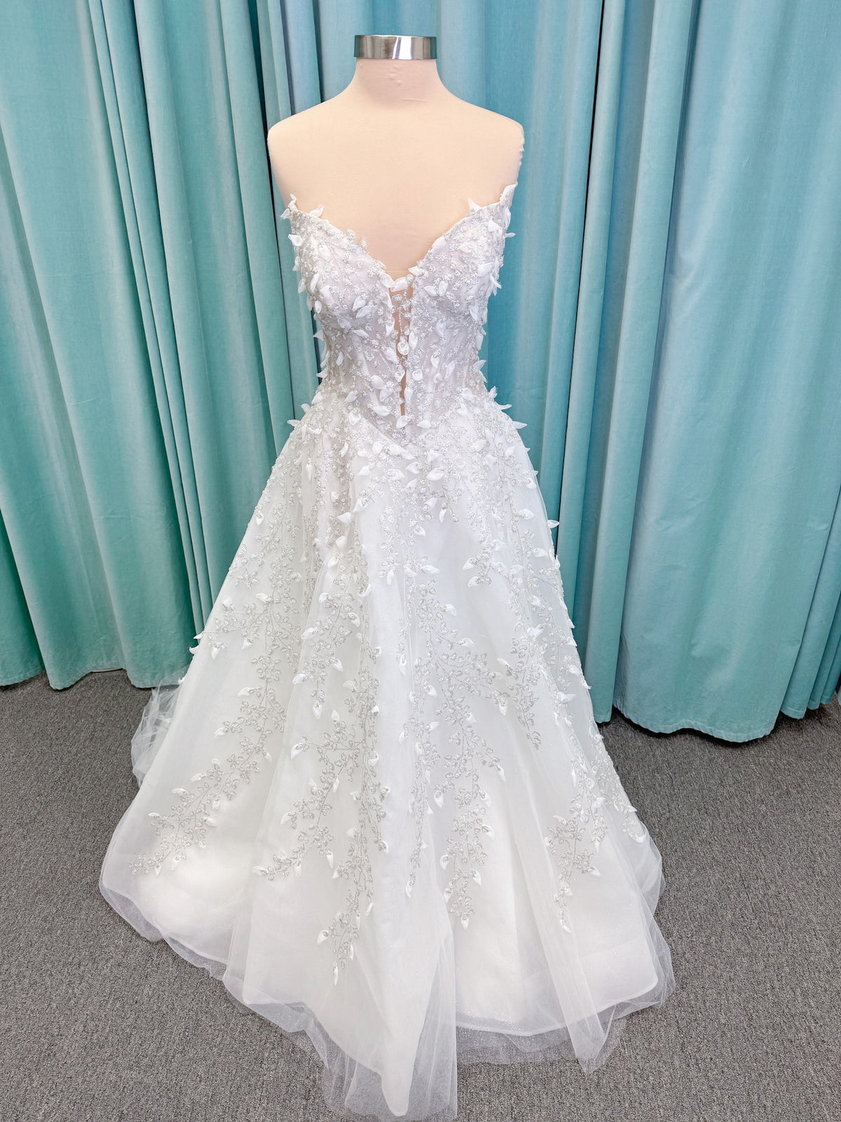 Randy Fenoli Goddess ballgown wedding dress on mannequin with plunging sweetheart neckline, 3D leaf appliqué, basque waist, high skirt slit, and sparkle tulle skirt