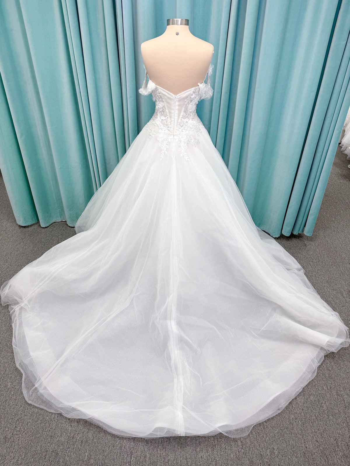 Randy Fenoli Indy A-line wedding dress on mannequin with off-the-shoulder sleeve drape, strapless sweetheart bodice, lace appliqué, basque waist, and high skirt slit