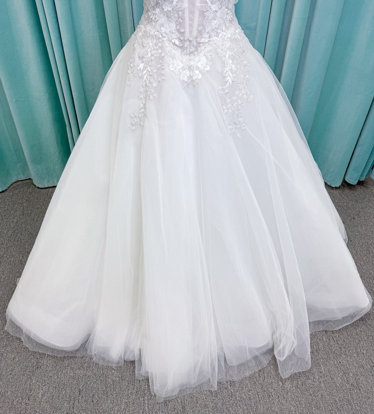 Randy Fenoli Indy A-line wedding dress on mannequin with off-the-shoulder sleeve drape, strapless sweetheart bodice, lace appliqué, basque waist, and high skirt slit