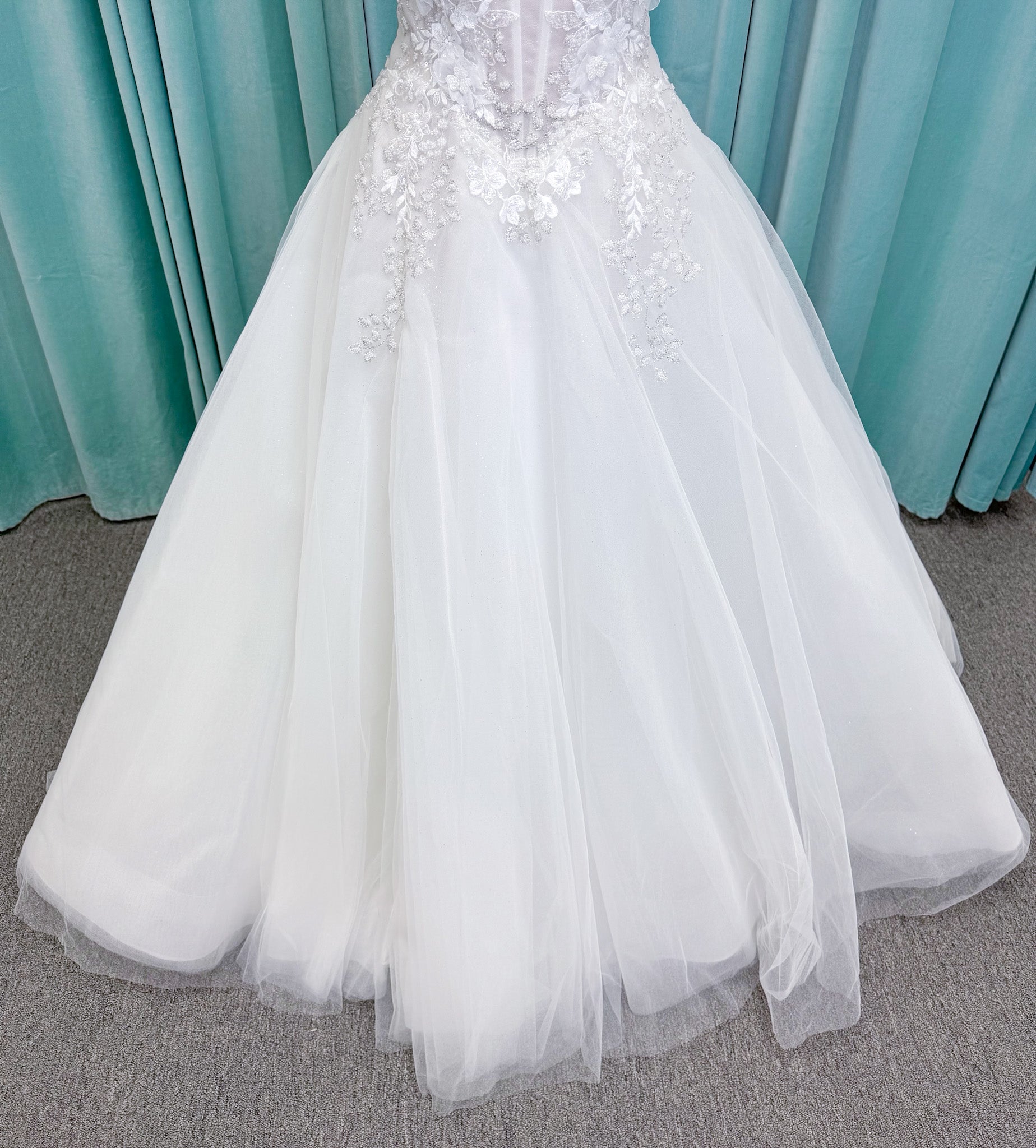 Randy Fenoli Indy A-line wedding dress on mannequin with off-the-shoulder sleeve drape, strapless sweetheart bodice, lace appliqué, basque waist, and high skirt slit