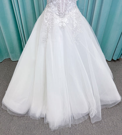 Randy Fenoli Indy A-line wedding dress on mannequin with off-the-shoulder sleeve drape, strapless sweetheart bodice, lace appliqué, basque waist, and high skirt slit