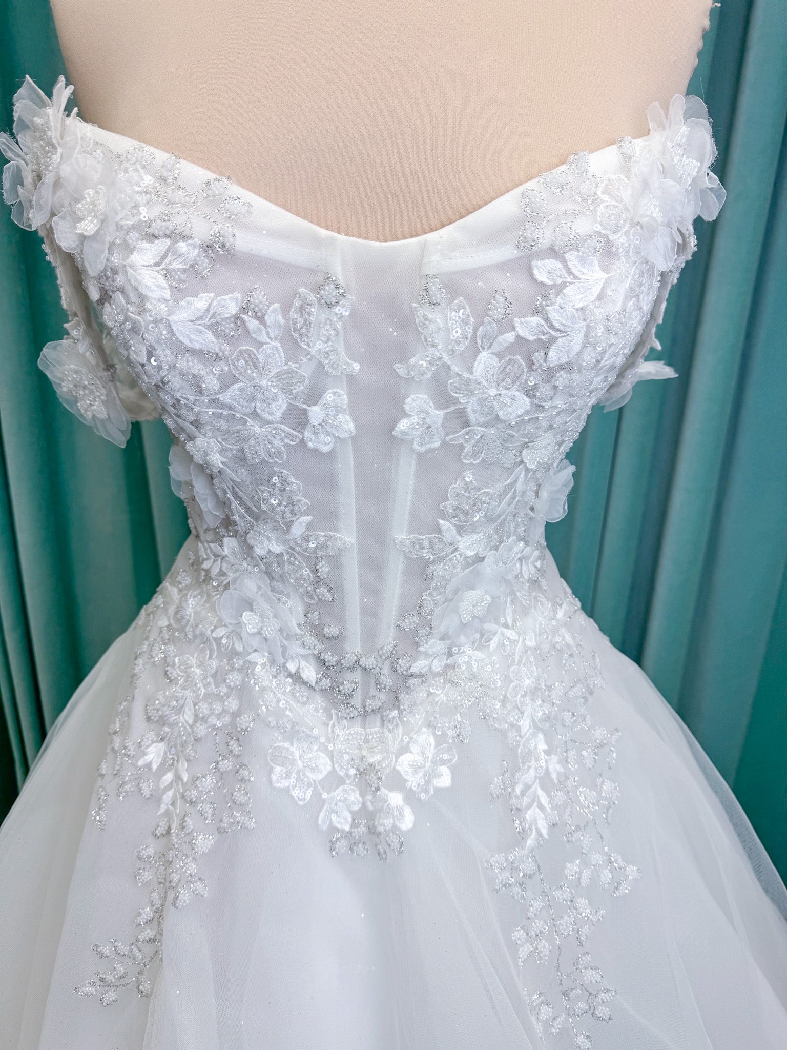Randy Fenoli Indy A-line wedding dress on mannequin with off-the-shoulder sleeve drape, strapless sweetheart bodice, lace appliqué, basque waist, and high skirt slit