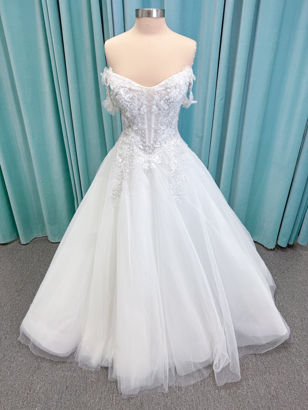 Randy Fenoli Indy A-line wedding dress on mannequin with off-the-shoulder sleeve drape, strapless sweetheart bodice, lace appliqué, basque waist, and high skirt slit
