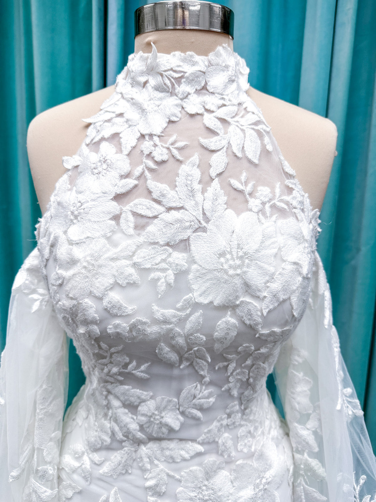 Morilee 2936 Kali fit and flare wedding dress on mannequin with high neckline, threadwork floral appliqued tulle, and detachable organza bow blouson sleeves