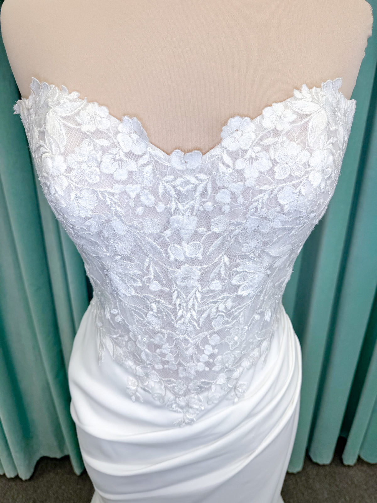 Randy Fenoli Kitty fit and flare wedding dress on mannequin with strapless sweetheart neckline, floral lace appliqué, and fluid crepe skirt