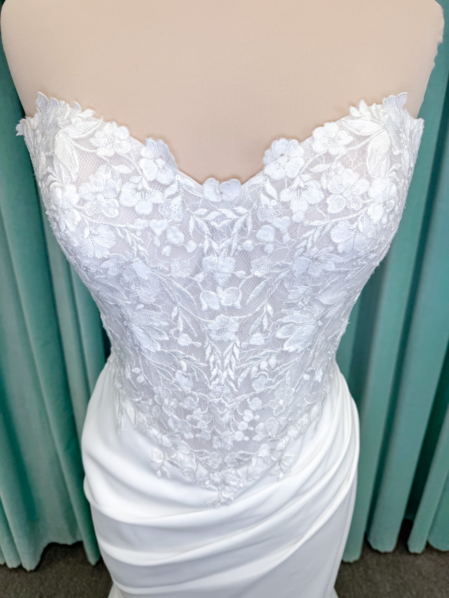 Randy Fenoli Kitty fit and flare wedding dress on mannequin with strapless sweetheart neckline, floral lace appliqué, and fluid crepe skirt