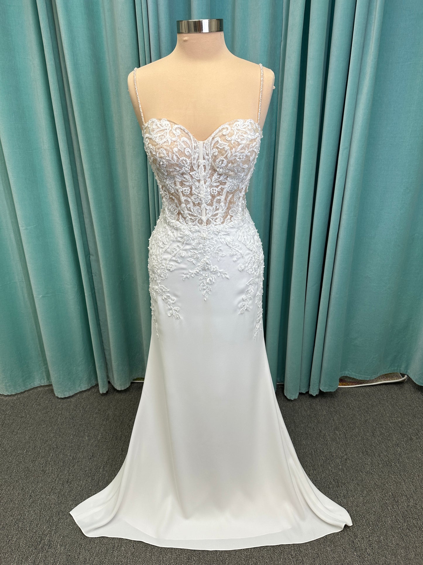Liena ivory spaghetti strap wedding dress on mannequin with illusion corset bodice, floral lace appliqués, sweetheart neckline, and crepe skirt.
