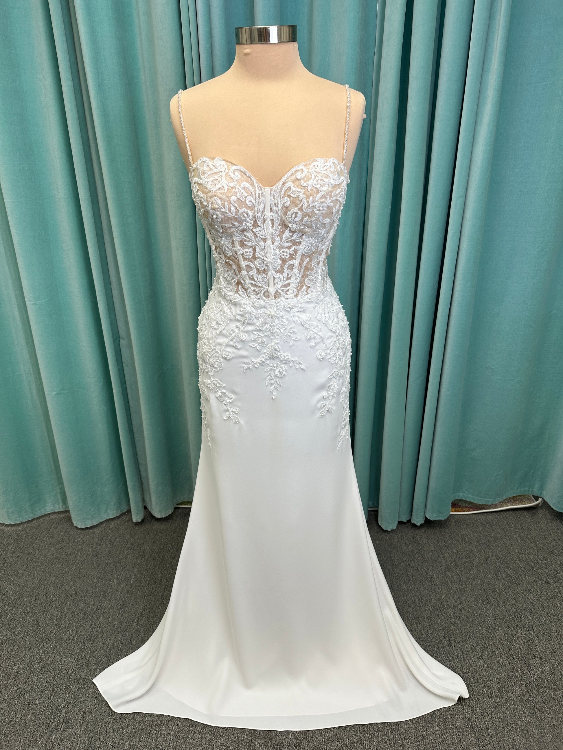 Liena ivory spaghetti strap wedding dress on mannequin with illusion corset bodice, floral lace appliqués, sweetheart neckline, and crepe skirt.
